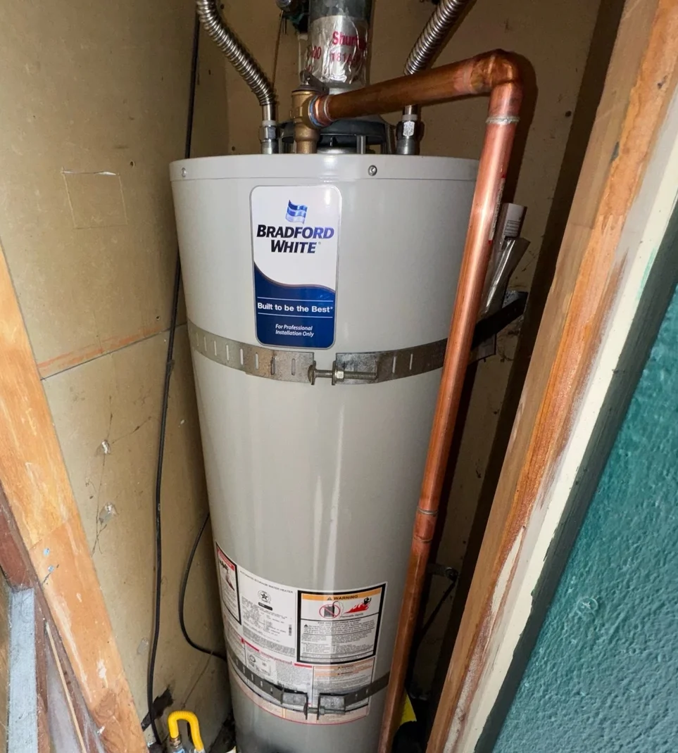 A Bradford White water heater in a utility closet with copper piping and gas lines, ready for use.